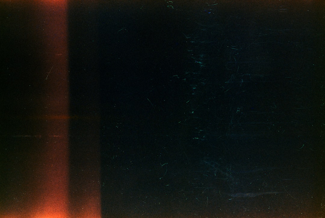 Dark background with a vertical orange light streak and dust.